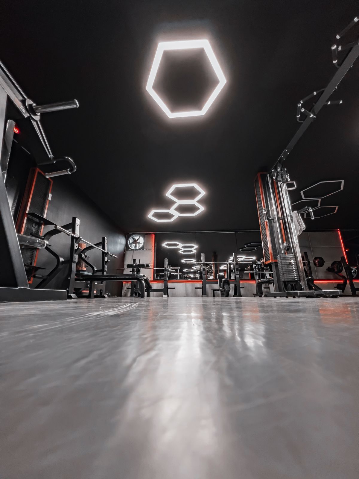 Dark weights room with racks, benches and hexagonal ceiling lights