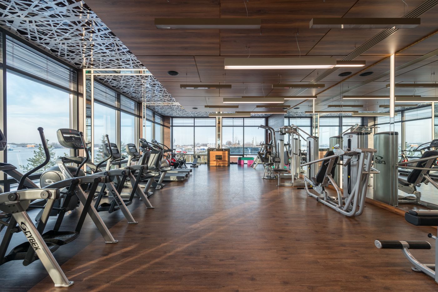 Gym floor with cardio machines beside floor-to-ceiling windows