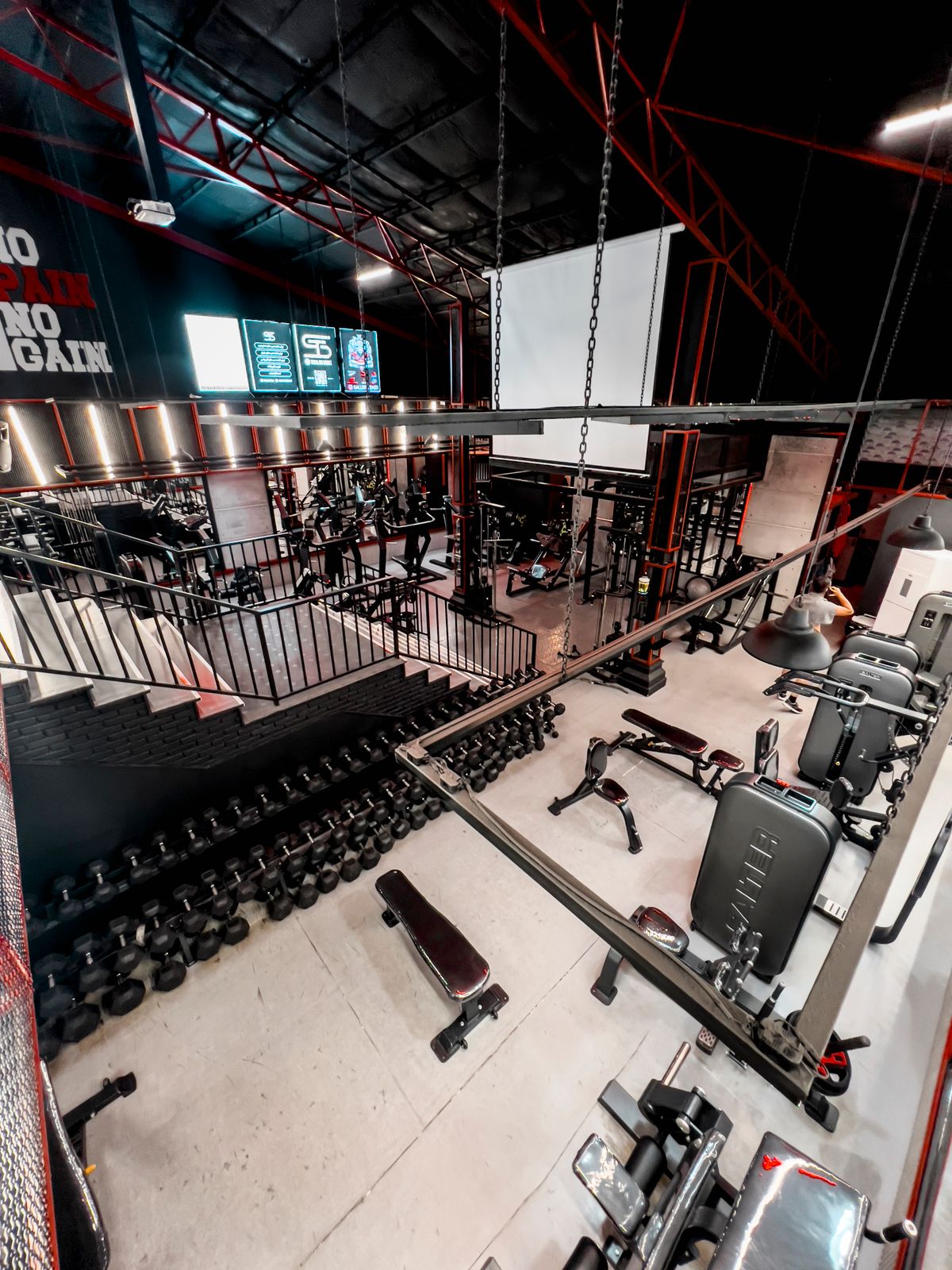 Two-storey gym floor with a long dumbbell rack and benches